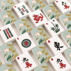 May include: A selection of white Mahjong tiles, each displaying red, green, and black symbols and numbers. Some tiles feature a red dragon, bamboo, or a floral design with a light blue background. The tiles are arranged in a grid pattern.