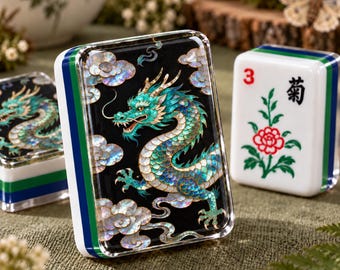 May include: A rectangular mahjong tile featuring a black surface with an iridescent mother-of-pearl dragon design surrounded by clouds. The tile has a white, blue, and green layered side profile. A second tile shows a red number 3 and a flower.