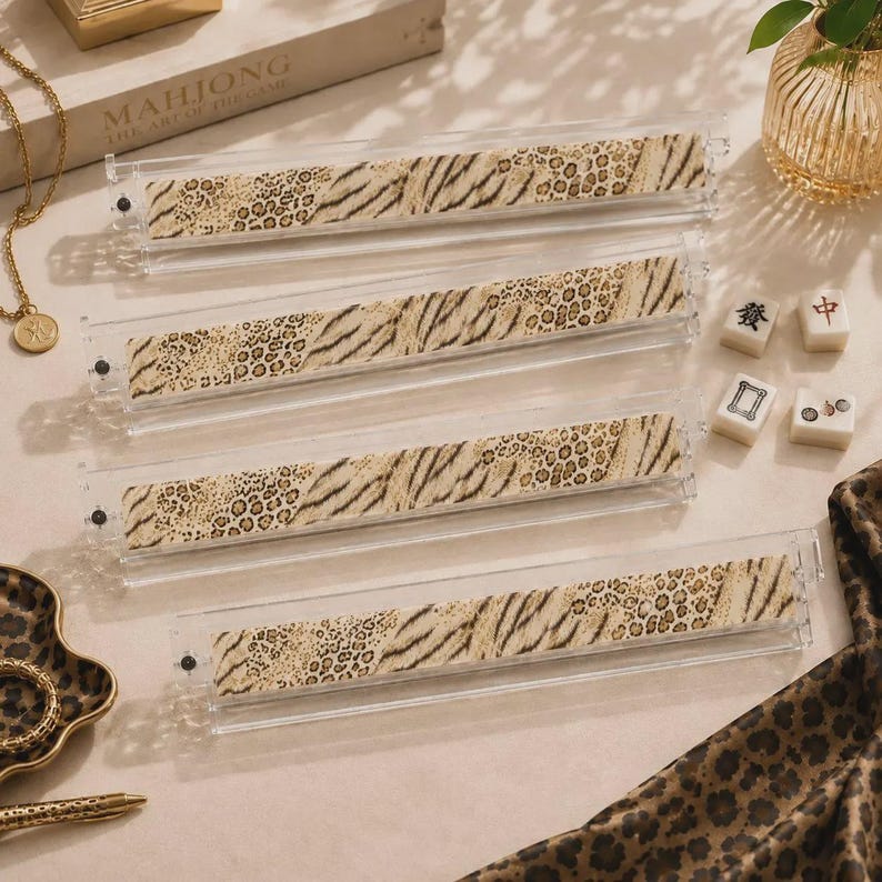 May include: Four clear acrylic mahjong tile racks featuring a beige and brown animal print pattern with leopard spots and tiger stripes. Each rack is rectangular and includes small metal hardware at the ends to secure the tiles during gameplay.