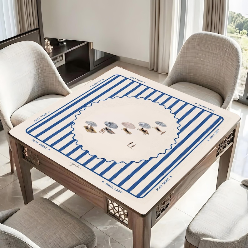 May include: A square wooden game table with a cream-colored top featuring blue stripes and a central design of figures under umbrellas. The table has a wooden frame and decorative cutouts on the sides. Chairs surround the table.