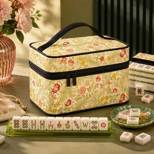 May include: A rectangular storage case with a floral pattern in shades of yellow, green, and red, featuring a black handle and zipper. The case is accompanied by a set of white mahjong tiles with green and red designs, displayed on a green rack.