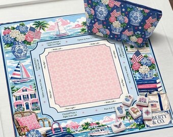 May include: A blue and white patterned cosmetic bag and a matching game board featuring coastal imagery, sailboats, and American flags. The board has a pink center and text that reads "Charleston" and "Hamptons Living."