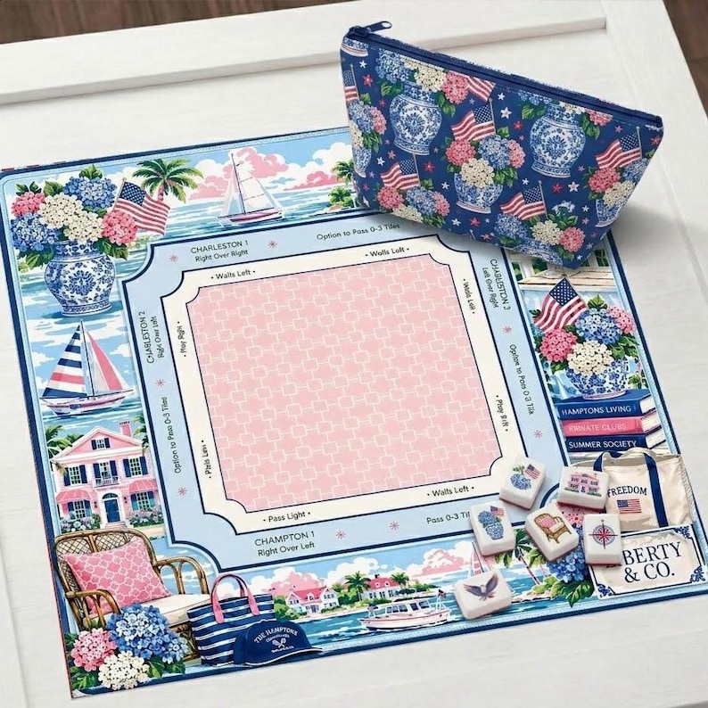 May include: A blue and white patterned cosmetic bag and a matching game board featuring coastal imagery, sailboats, and American flags. The board has a pink center and text that reads "Charleston" and "Hamptons Living."