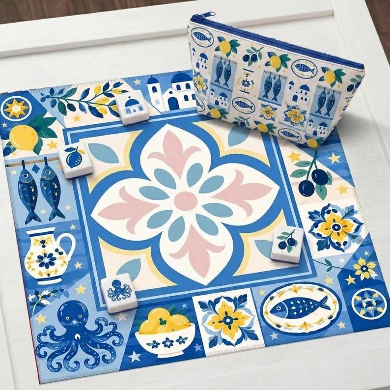 May include: A blue and white decorative mat with a floral and Mediterranean design, featuring lemons, fish, and octopus illustrations. A matching zippered pouch with a similar pattern is also present, along with several game tiles.