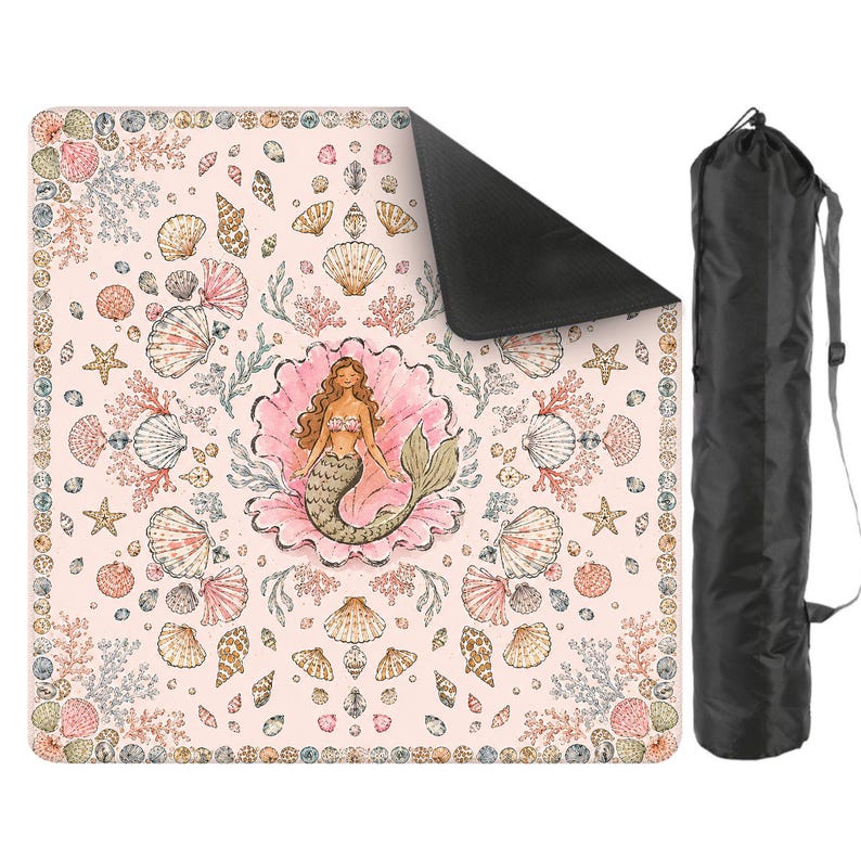 May include: A square picnic blanket with a light pink background featuring a central illustration of a mermaid inside a large seashell, surrounded by various seashells, starfish, and coral patterns, accompanied by a black cylindrical carrying bag.