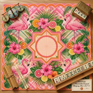 May include: A handmade tropical Mahjong mat, 31.5 inches square, featuring pink flamingos, hibiscus flowers, and citrus fruits. The mat has a central starburst design and includes Mahjong tiles and accessories. The text on the mat reads "Handmade Maximalist Tropical Mahjong Mat | 31.5" E".