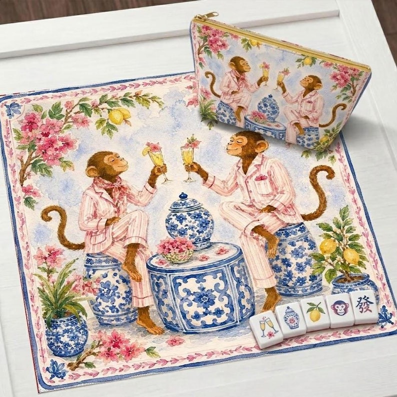 May include: A decorative set featuring a whimsical illustration of monkeys in pink pajamas toasting drinks. The set includes a square mat, a zippered pouch, and a few mahjong tiles. The design incorporates blue and white porcelain-style elements and floral accents.