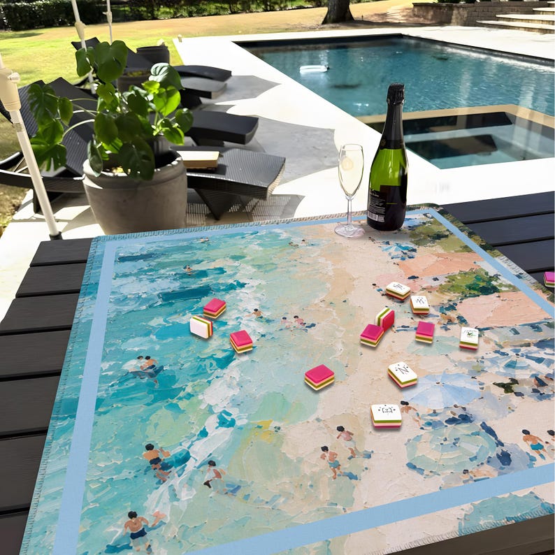 May include: A Mahjong set with a beach scene on the board. The board shows an ocean with swimmers. Pink and white tiles are scattered on the board. A bottle of champagne and a glass are also on the table.