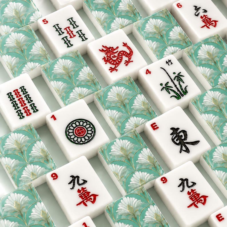 May include: A collection of white Mahjong tiles with red, green, and black symbols and characters. The tiles are arranged on a patterned background with a floral design in shades of teal and white. Some tiles feature a red dragon.