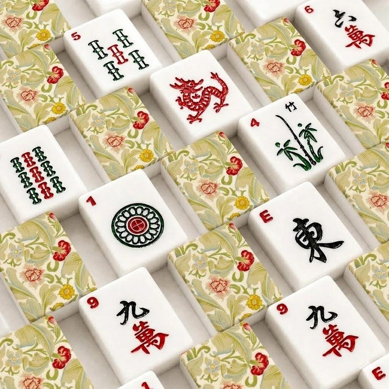 May include: A set of mahjong tiles featuring a mix of white tiles with traditional black, red, and green symbols and tiles decorated with a light green and beige floral pattern. The tiles display various characters, numbers, and a red dragon icon.