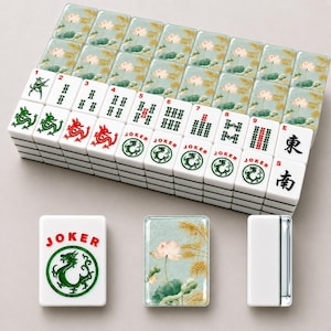 May include: A complete Mahjong set with white tiles featuring green and red symbols, numbers, and Chinese characters. The set includes tiles with a dragon and the word "JOKER". The tile box has a floral design.