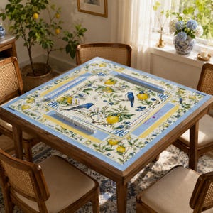 Puede incluir: Una mesa de mahjong cuadrada de madera con una parte superior decorativa con limones, p&aacute;jaros azules y motivos florales. La mesa est&aacute; rodeada de cuatro sillas de madera con respaldos tejidos. La mesa est&aacute; lista para un juego.