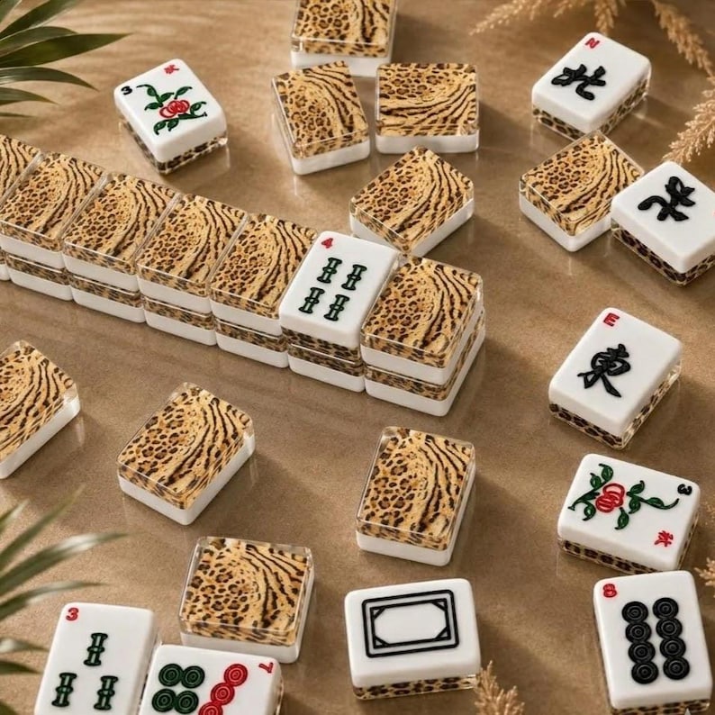 May include: A collection of rectangular mahjong tiles featuring white faces with black, red, and green ink symbols, including characters, circles, and floral designs. The backs of the tiles display a brown and black leopard print pattern.