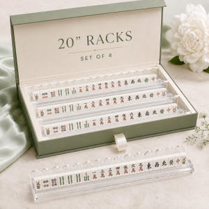 May include: A set of four 20-inch clear acrylic mahjong racks housed in a sage green storage box. The box lid features the text 20" RACKS SET OF 4. Each rack is filled with white mahjong tiles displaying various Chinese characters and symbols.