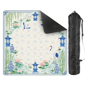 May include: A square outdoor picnic blanket featuring a blue and white pattern of cranes, lotus flowers, willow branches, and pagodas, with a black underside and a matching black cylindrical carrying bag with a shoulder strap for transport.