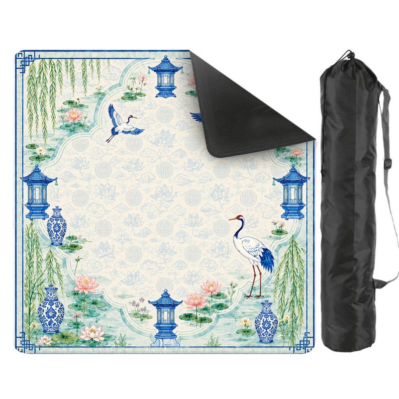 May include: A square outdoor picnic blanket featuring a blue and white pattern of cranes, lotus flowers, willow branches, and pagodas, with a black underside and a matching black cylindrical carrying bag with a shoulder strap for transport.