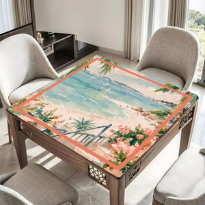 May include: A square wooden table with a beach scene painted on the top. The artwork features a sandy beach, turquoise water, and a blue sky. The table is surrounded by chairs.