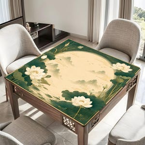 May include: A square table cover featuring a central cream-colored circle with a faint mountain landscape illustration. The border is deep green with large white lotus flowers and dark green lily pads. The table has a dark wood frame with cutouts.