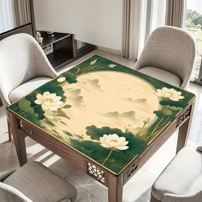 May include: A square table cover featuring a central cream-colored circle with a faint mountain landscape illustration. The border is deep green with large white lotus flowers and dark green lily pads. The table has a dark wood frame with cutouts.