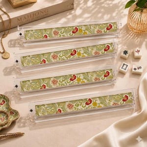May include: Four clear acrylic mahjong tile racks featuring a decorative insert with a light green background and a repeating floral pattern in shades of red, yellow, and cream. The racks are rectangular with small black end caps on each side.