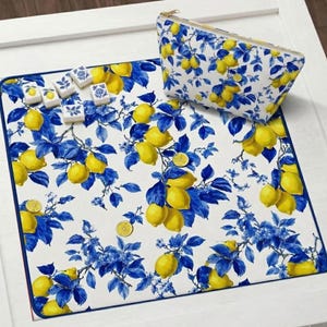 May include: A white mat and cosmetic bag with a lemon and blue floral design. The mat has a blue border and is covered in yellow lemons and blue leaves. The cosmetic bag has a gold zipper. Several decorative tiles are on the mat.