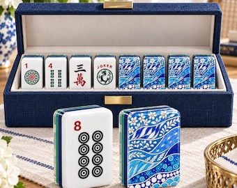 May include: A navy blue fabric-covered storage box containing a set of white mahjong tiles. The tiles feature red and black numbers, symbols, and a dragon graphic, while others display a blue and white floral and wave pattern on the back.