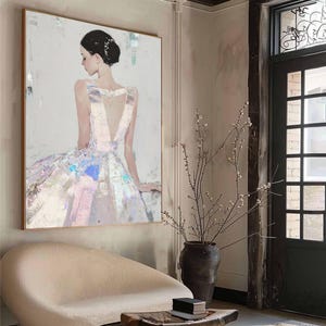 Puede incluir: Pintura abstracta de una mujer con un vestido fluido, en tonos pastel suaves. La obra presenta un escote en V profundo y una espalda baja, con acentos iridiscentes en la falda. La pintura est&aacute; enmarcada en un marco de madera dorada.
