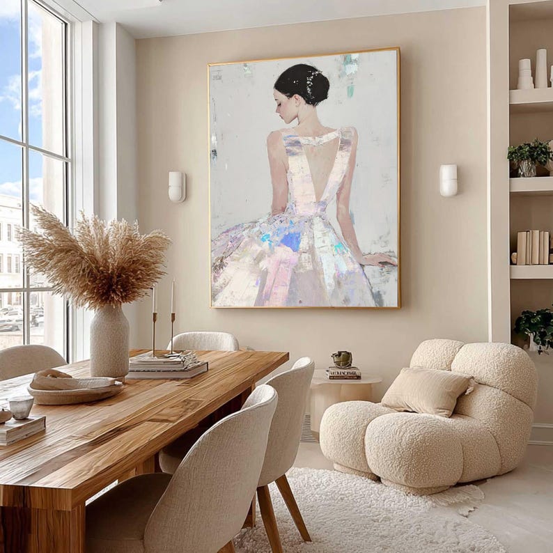 Puede incluir: Pintura abstracta de una mujer con un vestido blanco con la espalda baja, enmarcada en oro. La obra de arte cuelga sobre una mesa de comedor de madera con sillas beige. Un sill&oacute;n esponjoso de color crema y un jarr&oacute;n con hierba de la pampa seca completan la decoraci&oacute;n de la habitaci&oacute;n.