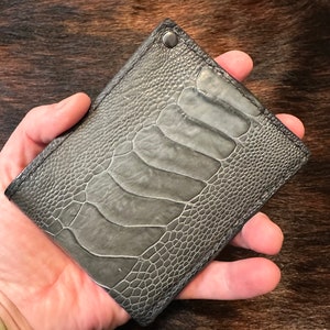 May include: A gray ostrich leather wallet with a single silver rivet.