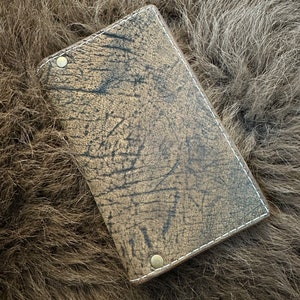 May include: A brown leather wallet with a distressed finish and white stitching. The wallet has two brass rivets on the front.