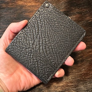 May include: A black leather wallet with a textured surface and a silver rivet.