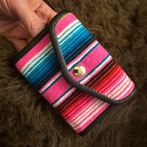 May include: A small pink and blue striped wallet with a black leather flap and a silver snap closure.