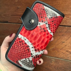May include: A red and white snakeskin wallet with a black leather flap and a skull-shaped metal clasp.