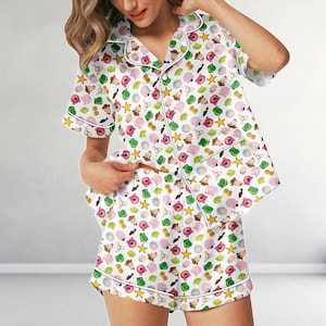 May include: White pajama set with a colorful pattern of cartoon characters. The short-sleeved top and shorts have white piping and a button-down front. The pattern includes stars, aliens, and other characters.