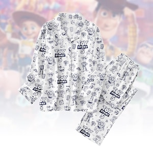 May include: White pajama set featuring a repeating pattern of Toy Story characters and the text "TOY STORY 5". The set includes a button-down top and matching pants. The pajama set is a comfortable sleepwear option.