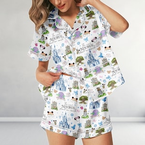 May include: White pajama set with a whimsical print featuring castles, rainbows, and the text "The most MAGICAL place on earth." The set includes a short-sleeved top and shorts, both trimmed with white piping.