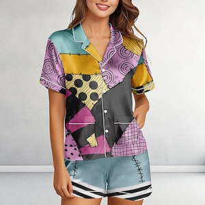 May include: A short-sleeve button-down pajama shirt and matching shorts set featuring a patchwork design. The pattern includes yellow, purple, pink, and light blue sections with various prints like polka dots, swirls, and grids, accented by black stitch lines.