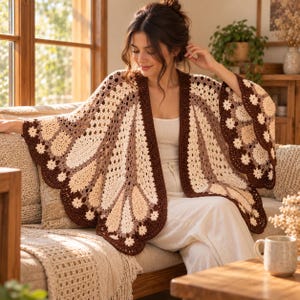 May include: A crochet butterfly wing shawl featuring a color palette of dark brown, light brown, and cream. The garment is constructed with intricate openwork patterns and scalloped edges, designed to drape over the shoulders and arms.