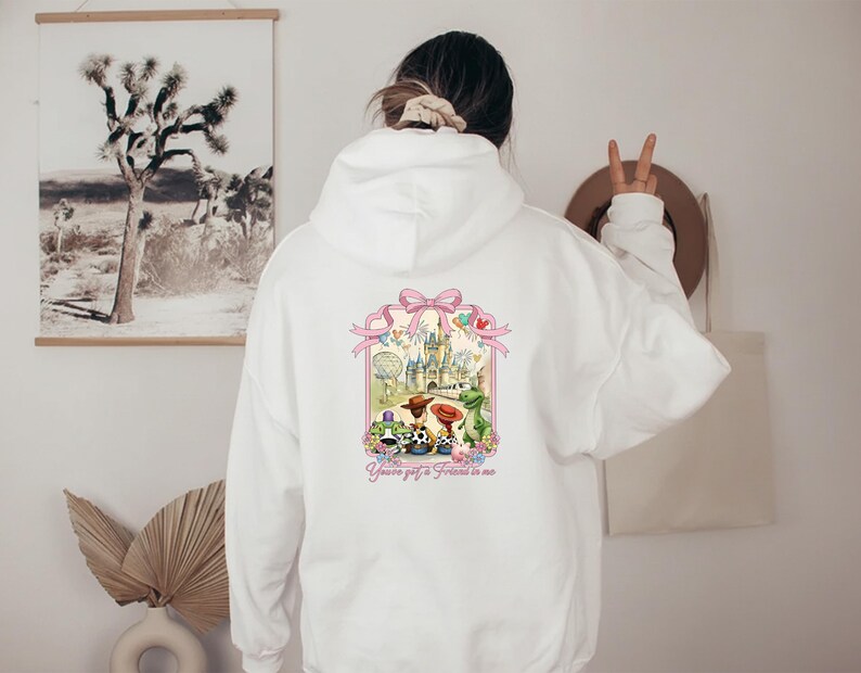 May include: White hoodie with a colorful graphic on the back featuring a castle, characters, and the text "You've got a friend in me." The graphic is framed by a pink bow and ribbon design.