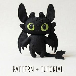 May include: A black dragon plush toy with large green eyes, wings, and a tail. The dragon is standing on a white surface. The text "PATTERN + TUTORIAL" is below the dragon.