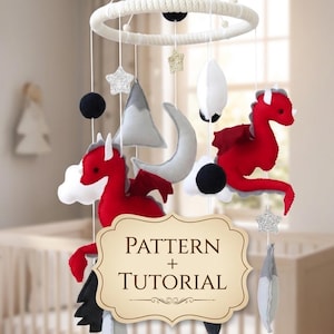 Può includere: Un mobile per bambini fatto a mano con draghi di feltro rosso, nuvole bianche e montagne grigie sospese da un anello bianco. Il mobile include stelle, lune e un cartello con "PATTERN + TUTORIAL".