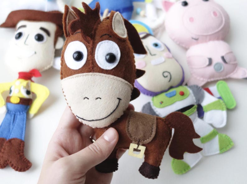 May include: Handmade felt plush toys of characters from the animated movie Toy Story. The toys include a brown horse, Woody, Buzz Lightyear, and others. The horse has a light tan muzzle and a brown saddle.