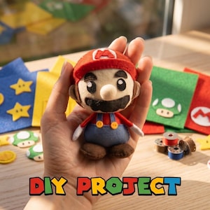 Puede incluir: Una muñeca de fieltro de Mario, con gorra roja y peto, se sostiene en una mano. Accesorios de fieltro, incluyendo estrellas, champiñones y bloques de interrogación, están dispersos. El texto "DIY PROJECT" está en la parte inferior.