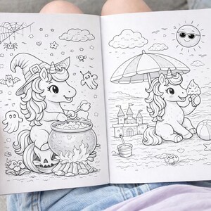 May include: A coloring book open to two pages with unicorn illustrations. One page shows a unicorn in a witch hat stirring a cauldron. The other page shows a unicorn at the beach with an ice cream cone. The book is held open by a person.