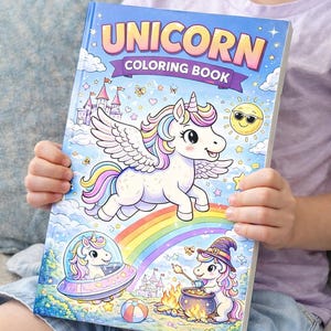 May include: A colorful unicorn coloring book with the title "UNICORN COLORING BOOK" on the cover. The cover features a winged unicorn, a rainbow, a smiling sun, and other whimsical illustrations. The book is held by a person.