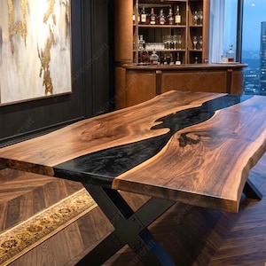 Op de afbeelding: Een grote eettafel van massief hout met een zwarte epoxy rivier in het midden. De tafel heeft een donkere houten afwerking en staat op een zwart metalen X-vormig onderstel. De tafel staat in een moderne eetkamer.