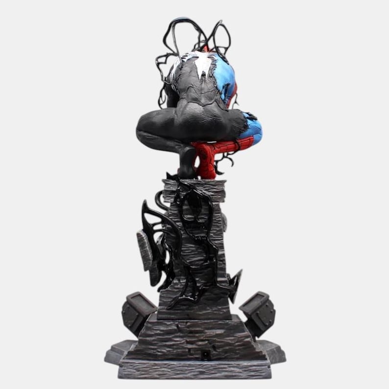 May include: A detailed figurine of a superhero, featuring a black and gray body with blue and red accents. The figure is perched atop a textured, dark gray pedestal with black, organic-looking embellishments. The overall design suggests a comic book or fantasy theme.