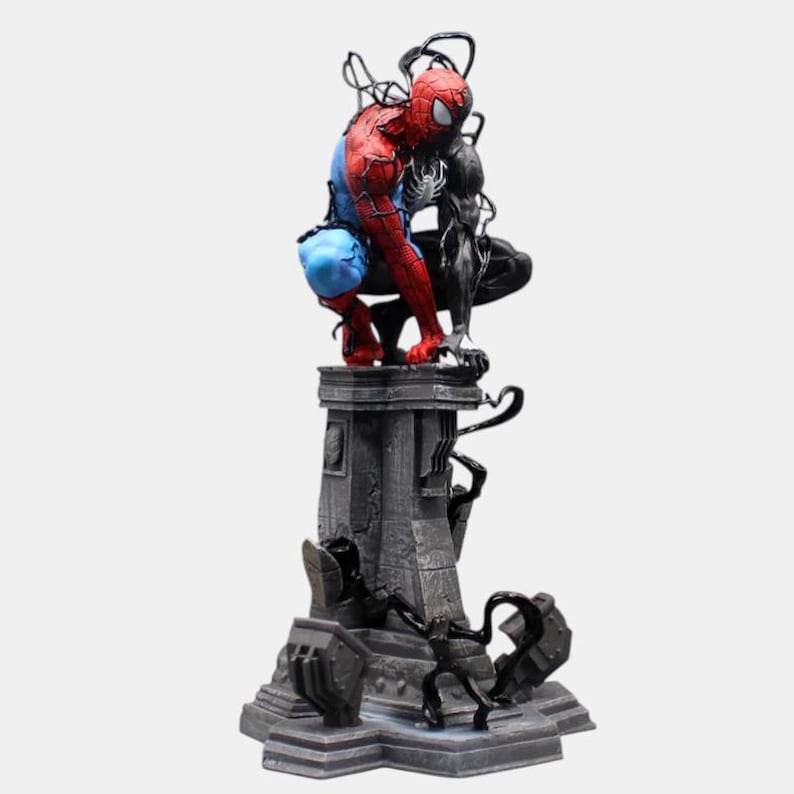 May include: A detailed figurine of Spider-Man in a crouched position, with a black Venom figure beside him. The Spider-Man figure is in his classic red and blue suit. The base is a gray, detailed pedestal.