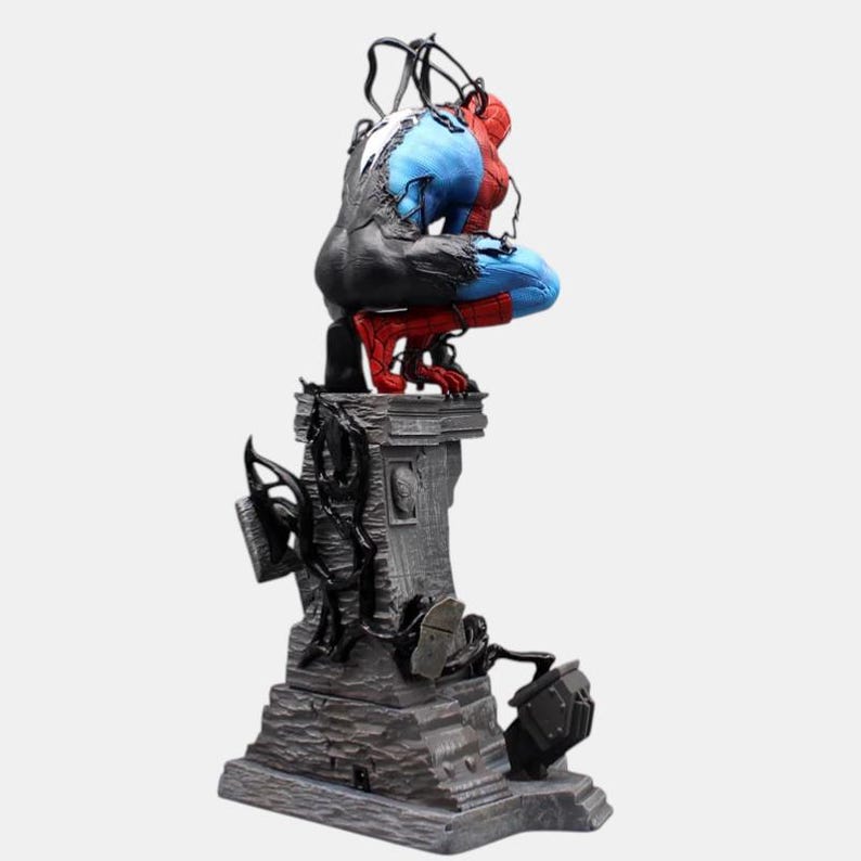 May include: A detailed statue of a superhero figure, half in red and blue, the other half in black. The figure is crouched atop a gray stone pedestal with intricate details and black tendrils. The statue is a collectible item.