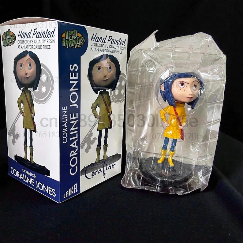 May include: A Coraline Jones bobblehead figure in a clear plastic case next to a box. The figure wears a yellow raincoat, blue hair, and black boots. The box features the figure and the text "CORALINE JONES" and "Hand Painted".